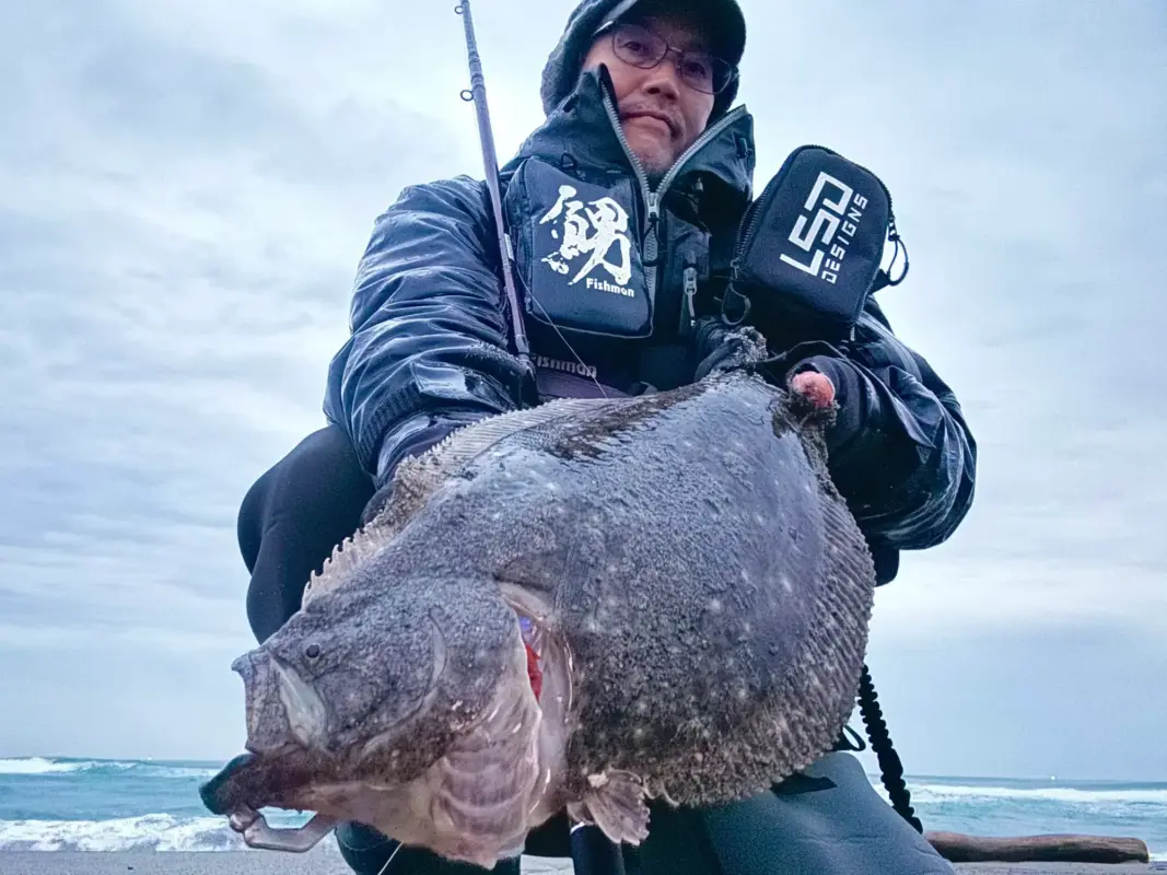 サーフで釣り上げた大型のヒラメを持つアングラー